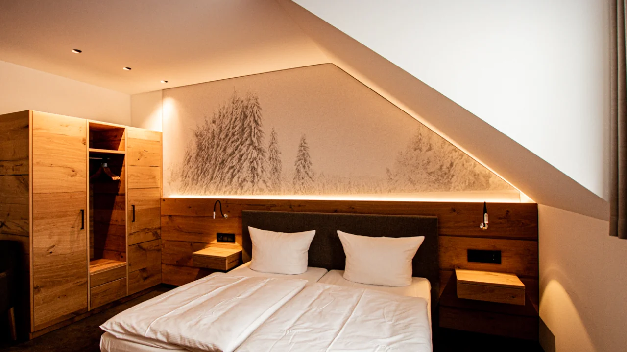 Hotelzimmer im Schlafbereich mit großformatigem Akustikbild einer Winterlandschaft über dem Bett, integriert in Holzvertäfelung und Dachschräge