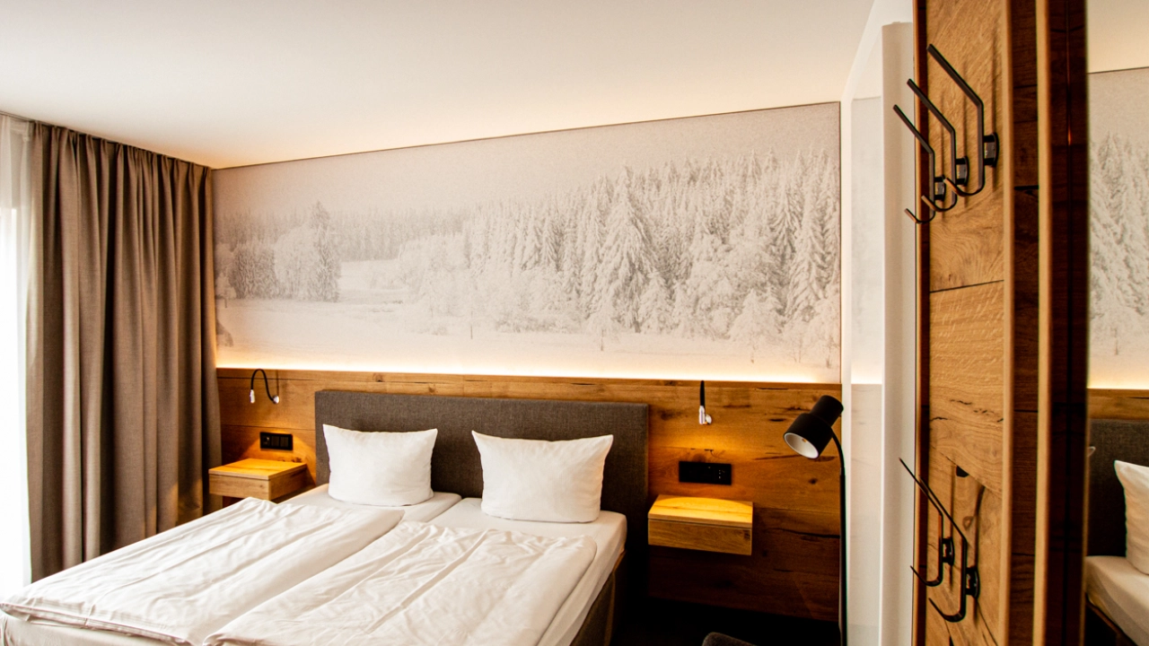 Gesamtansicht eines Hotelzimmers mit Akustikbild einer Winterlandschaft über dem Doppelbett und warmer indirekter Beleuchtung